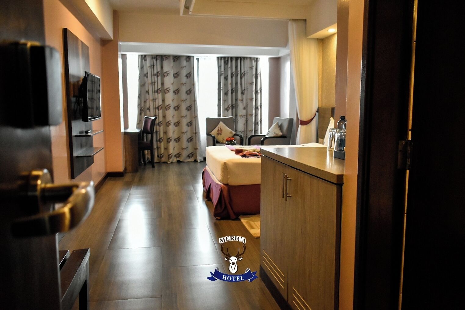 A hotel room with a bed, a desk, a chair, a TV, and a window with curtains.