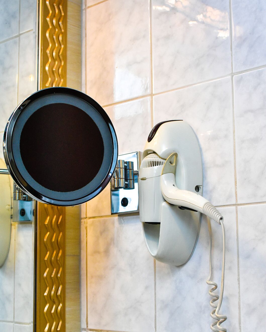 A hairdryer mounted on a tiled wall with a mirror above it.