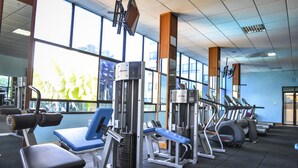 A gym with various exercise equipment, large windows, and a high ceiling.