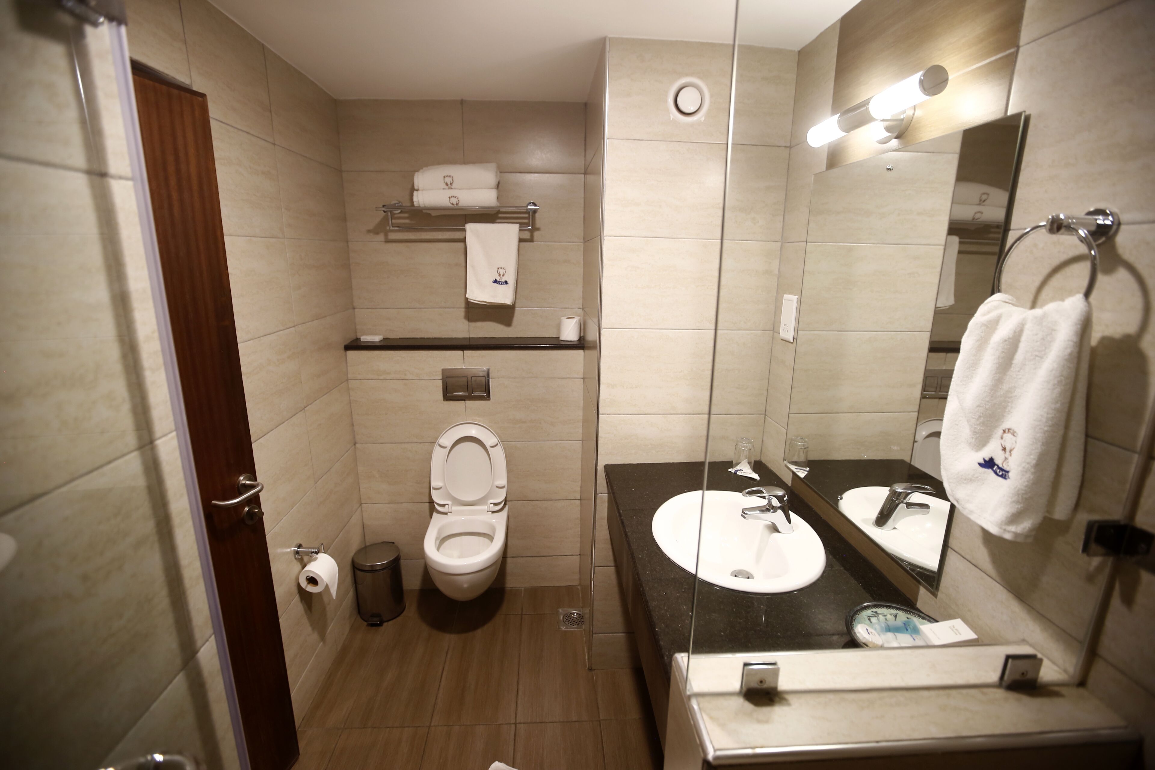 A modern bathroom with a toilet, sink, mirror, towel rack, and a trash bin.