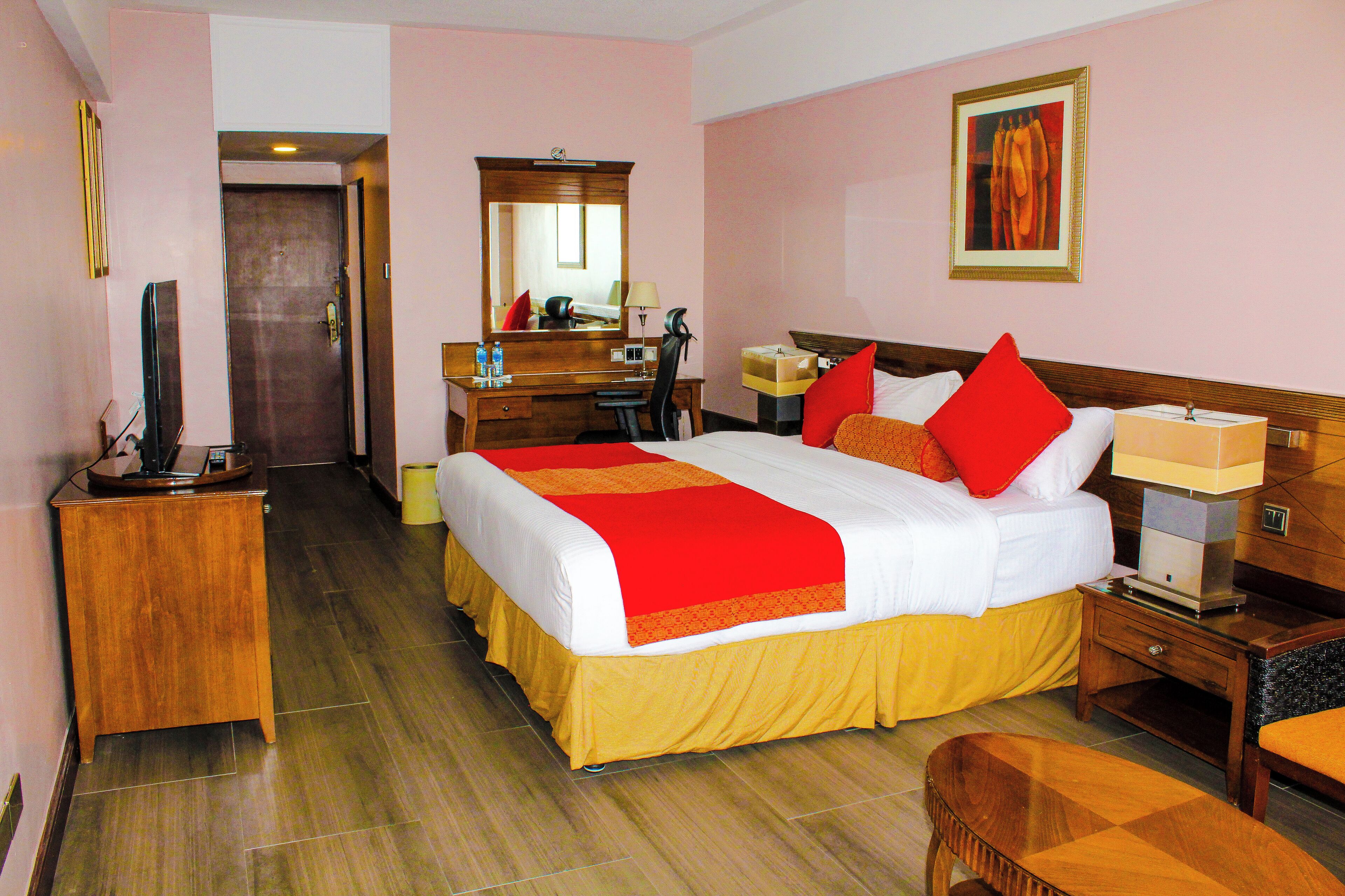 A hotel room with a large bed, a desk, a chair, a dresser, a mirror, and a painting on the wall.