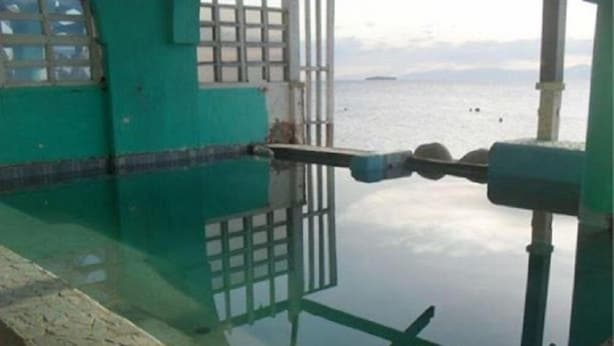 A view of a calm body of water with a distant ship, a green building with a window, and a metal structure in the foreground. - Anthonys Beach Resort (Moalboal)