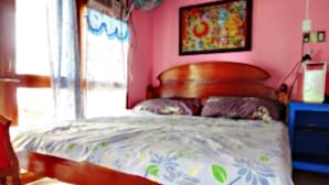 A bedroom with a wooden bed frame, floral bedding, a colorful painting on the wall, and a blue nightstand with a lamp. - Anthonys Beach Resort (Moalboal)
