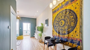 Un comedor con una mesa dispuesta para dos, un tapiz en la pared y una planta en la esquina.