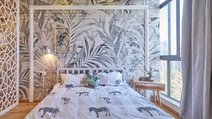 Un dormitorio con cubrecama con motivos de cebra, un mural de follaje en la pared, una mesita de noche de madera y una ventana con vistas a edificios.
