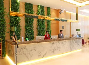 A reception desk with a marble top, surrounded by vertical green plant walls, and equipped with computers and a telephone. - Nan He Xi Yue Hotel (Chengdu)
