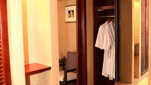 Une chambre d’hôtel avec une armoire en bois, un miroir et une robe blanche accrochée.