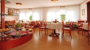 A dining area with multiple tables and chairs, a buffet with various food items, and a ceiling light fixture. - Hotel Haus Am Steinberg (Bad Driburg)