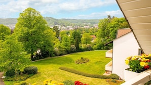 A garden with a lawn, a circular flower bed, and a white building with a balcony. - Hotel Haus Am Steinberg (Bad Driburg)