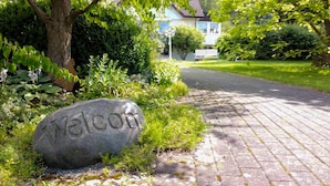 A stone welcome sign on a brick pathway leading to a house with a blue roof. - Hotel Haus Am Steinberg (Bad Driburg)