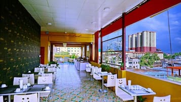 A restaurant with tables and chairs, a tiled floor, and a view of buildings through large windows.