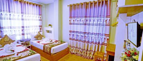 A hotel room with two beds, a wooden floor, a small wooden stool, a TV, and a flower arrangement.