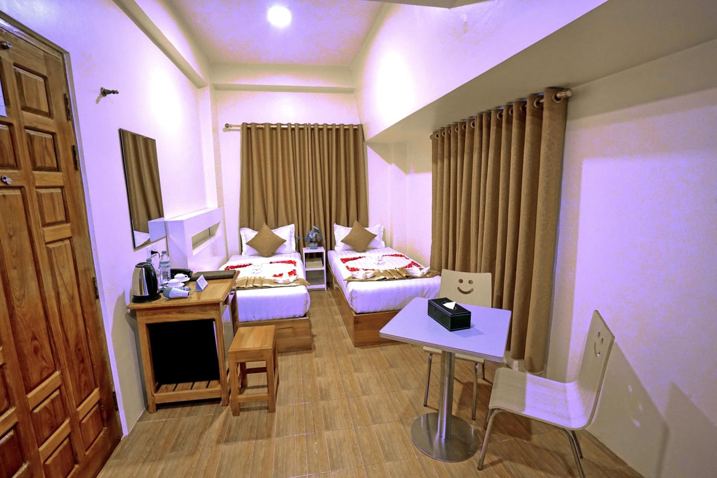 A hotel room with two beds, a small desk, a chair, a table, and a mirror.