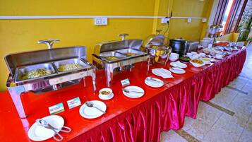 Een buffetopstelling met meerdere stations voor eten en bestek, uitgestald op een rode tafelkleed.