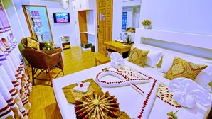 A hotel room with a bed, a sitting area with a chair and table, a television, and a bathroom visible through an open door. - Hotel Aurora (Mandalay)