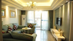 A modern living room with a green sofa, a small round table, a TV mounted on the wall, and a large window with curtains. - Chengdu Charm City Hotel (Chengdu)