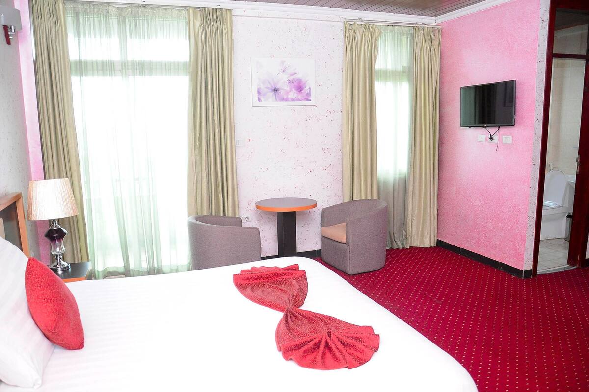 A hotel room with a bed, a desk, a chair, a TV, and a bathroom.