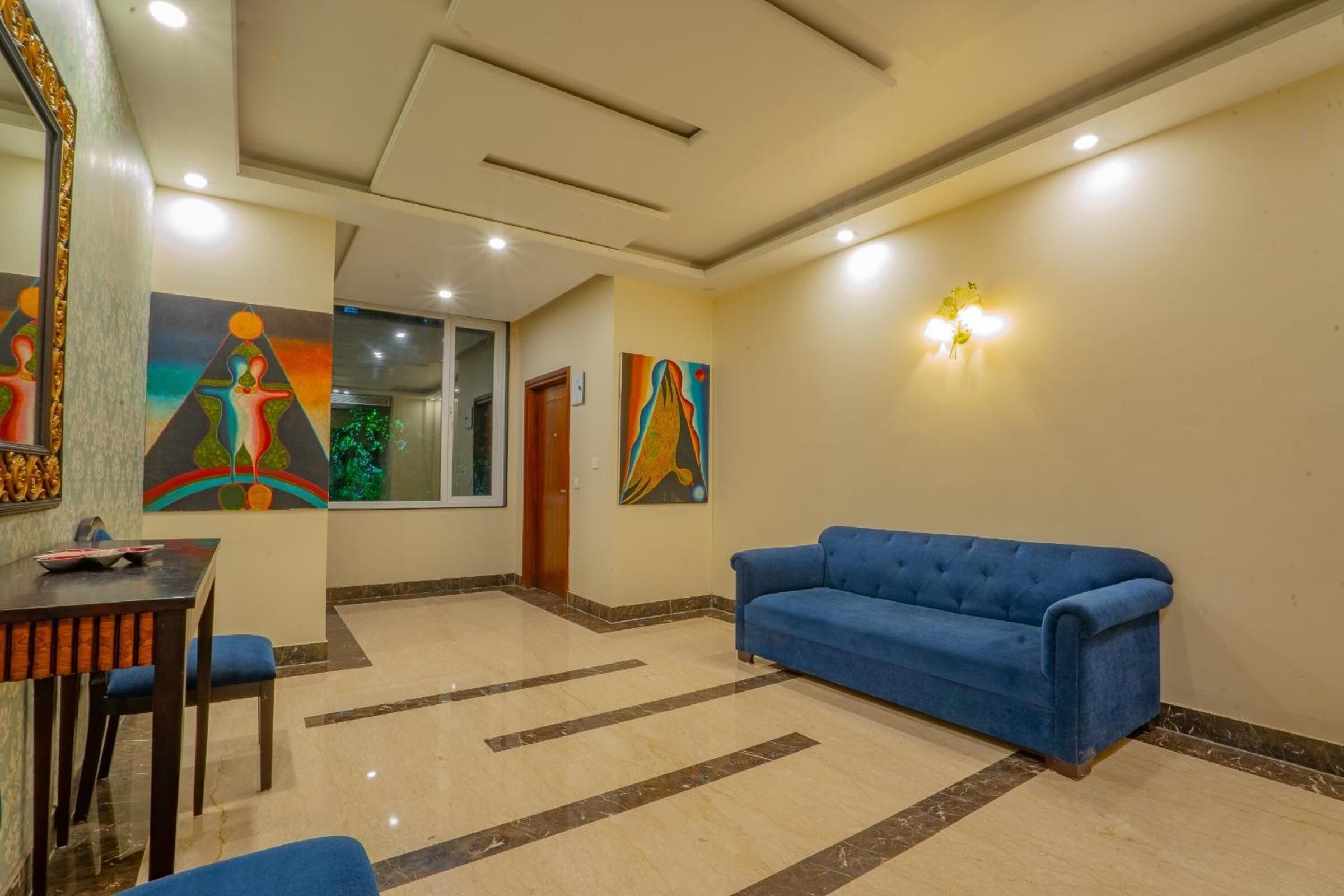 A hotel lobby with a blue sofa, a wooden table with chairs, and colorful artwork on the walls.