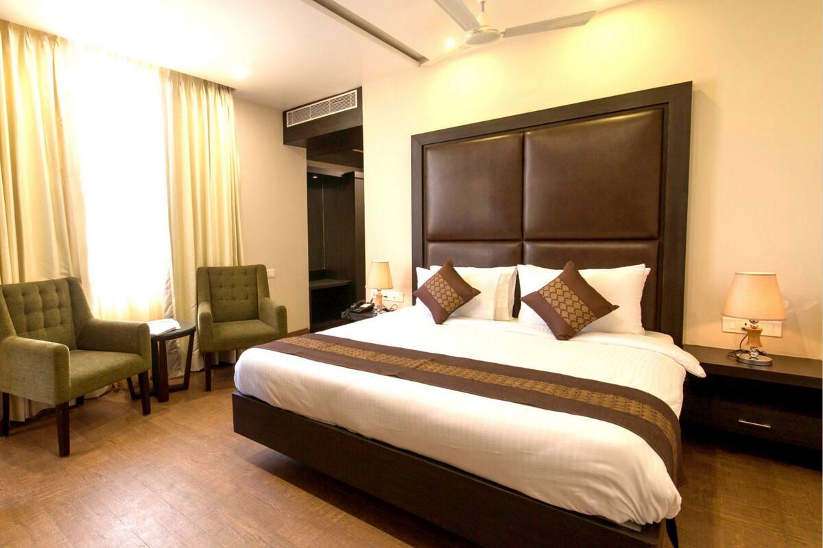 A hotel room with a large bed, two armchairs, a small table, a desk, a lamp, and a ceiling fan.