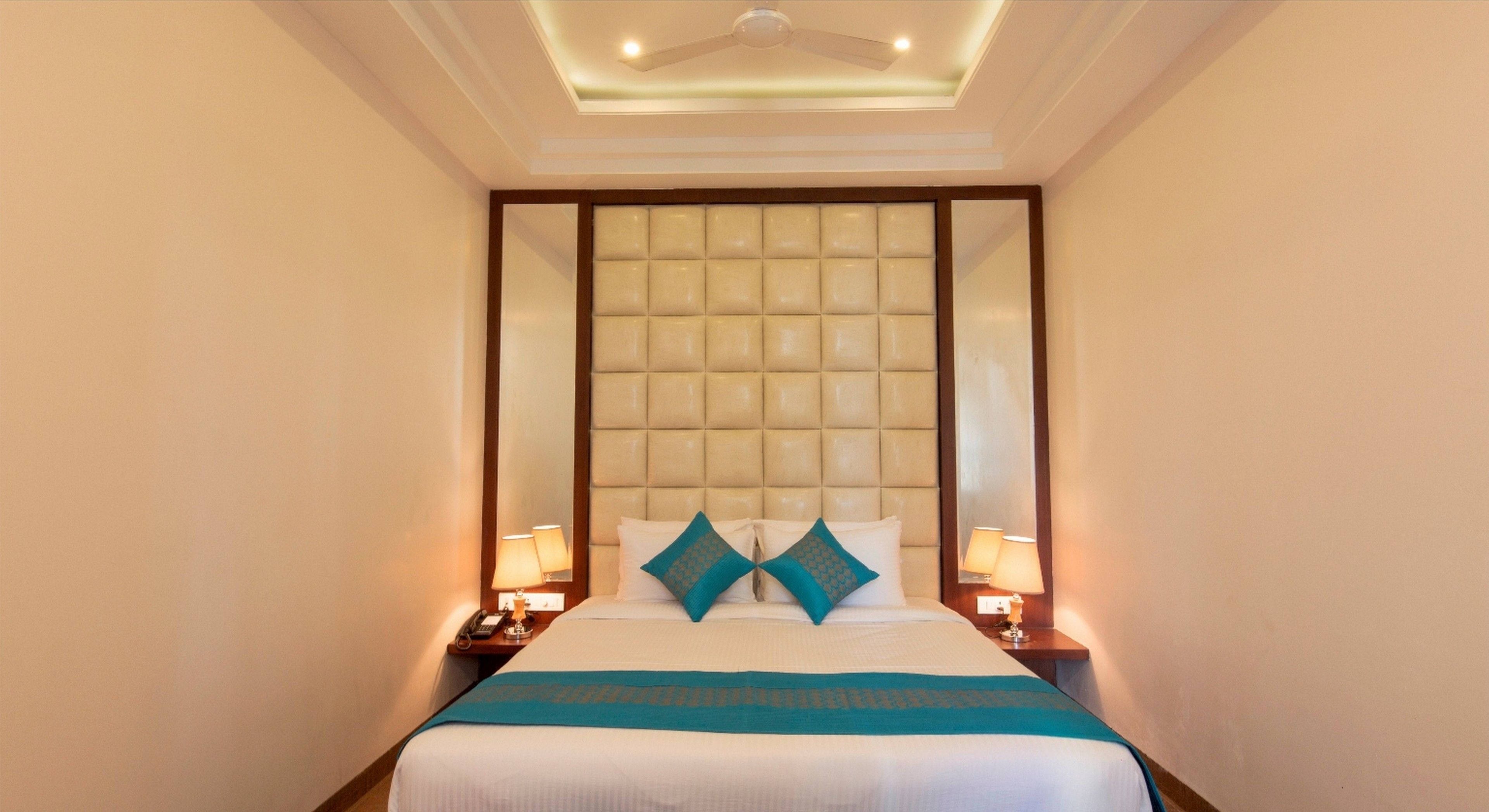 A hotel room with a large bed, two nightstands, a ceiling fan, and a padded headboard.
