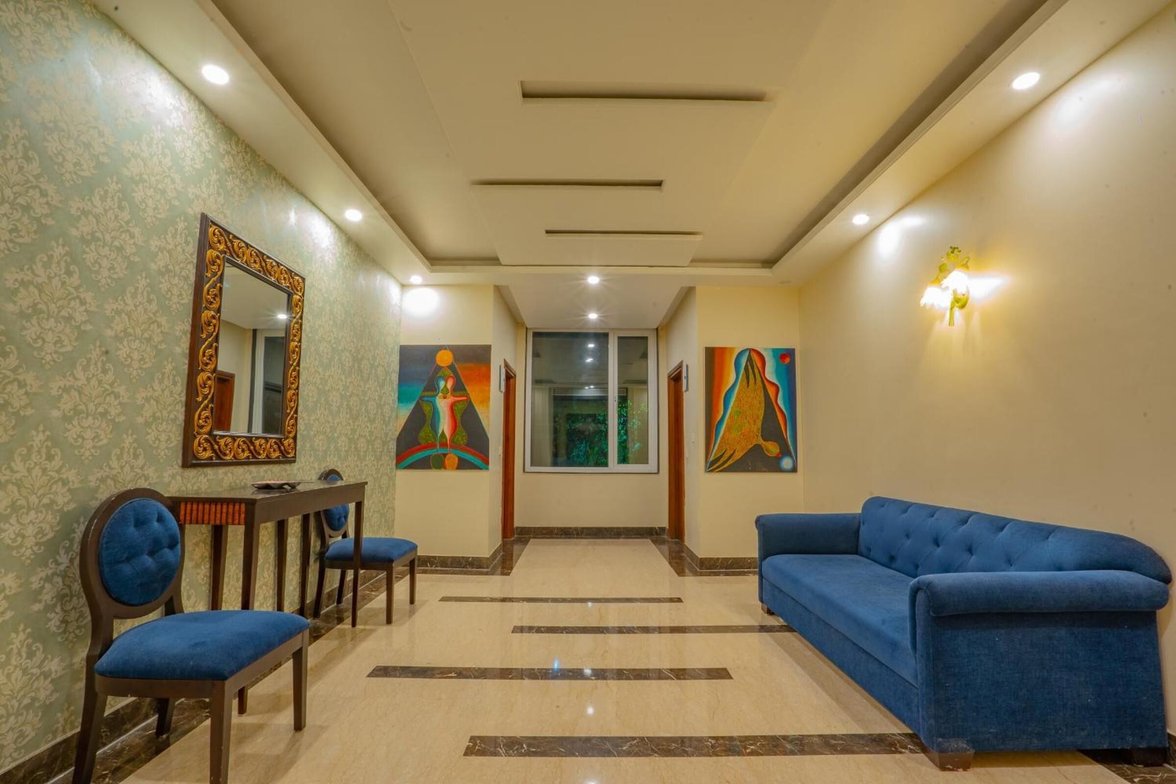 A hotel lobby with a blue sofa, a wooden table with chairs, and two paintings on the walls.