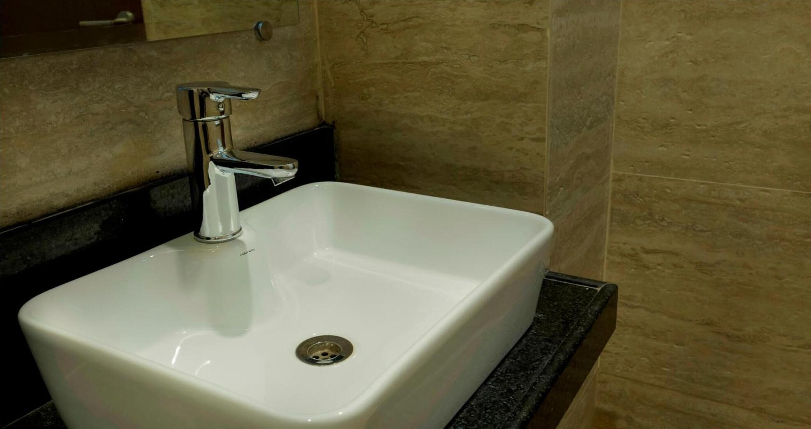 A white bathroom sink with a chrome faucet, set against beige tiled walls.