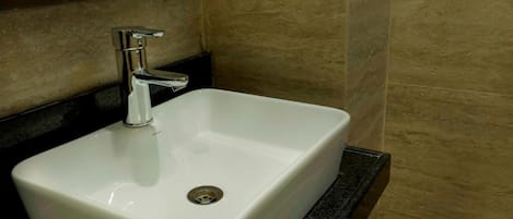 A white bathroom sink with a chrome faucet, set against beige tiled walls.