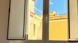 A hotel room with a bed, a window with a view of the outside, and a radiator below the window. - Termini Station Little House (Rome)
