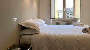 A hotel room with a bed, two wall-mounted lamps, a window with an open view, and a radiator. - Termini Station Little House (Rome)