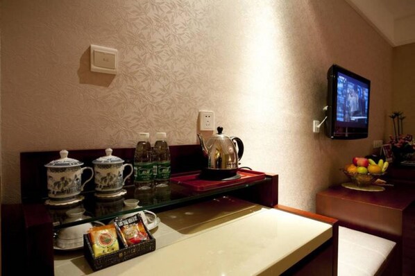 A hotel room with a kitchen area, including a coffee maker, tea set, and a fruit bowl.