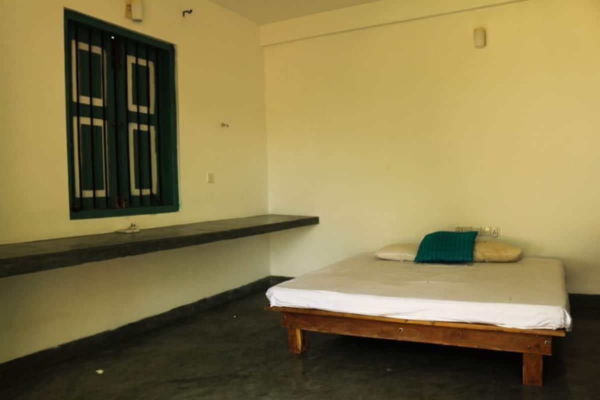 A room with a bed, a window with bars, a shelf, and a light switch on the wall.
