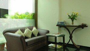 A living room with a brown sofa, a small round table, and a potted plant. - Nangi's Pride (Jaipur)