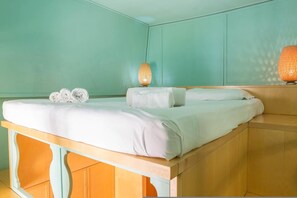 A neatly made bed with white linens and rolled towels, a wooden headboard, and a wall-mounted lamp. - Friendly Domus al Colosseo (Rome)