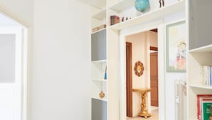 A hallway with a white door, a bookshelf with books and decorative items, and a framed picture on the wall. - Flaminio & Popolo Large Apartment (Rome)