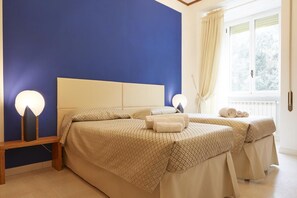 A bedroom with two beds, a nightstand, and a window with curtains.