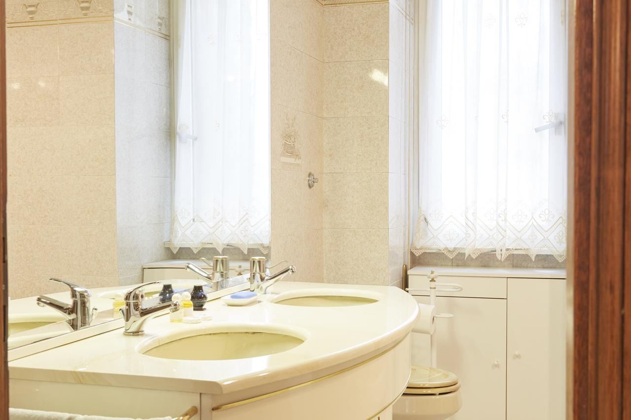 A bathroom with two sinks, a toilet, and a window with curtains.