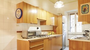 A kitchen with wooden cabinets, a built-in oven, a refrigerator, and a window with decorative ironwork. - Flaminio & Popolo Large Apartment (Rome)