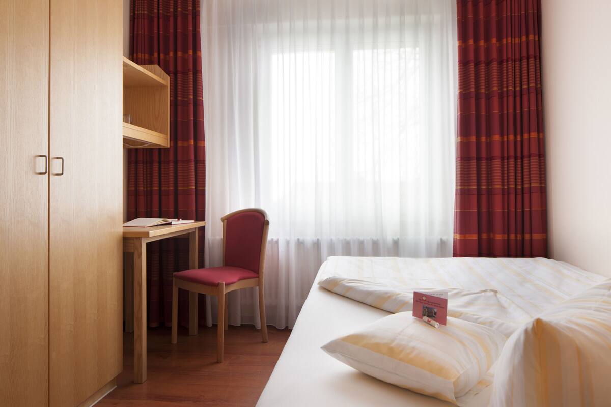 Una habitación de hotel con una cama, un escritorio, una silla y un armario.