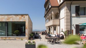 Een buitenruimte met tafels en stoelen, omgeven door gebouwen met traditionele architectuur en een helder uitzicht op het landschap.