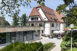 Un bâtiment moderne doté d’un toit en pente, de grandes fenêtres et d’un espace extérieur aménagé pour s’asseoir.