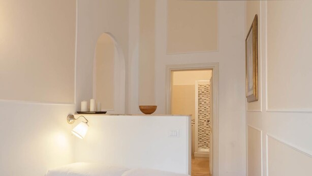 Quarto de hotel com uma cama, uma luminária fixada na parede, uma tigela de madeira e um papel de parede estampado.