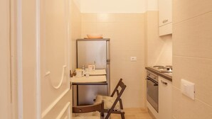 Uma cozinha compacta com geladeira, fogão e um pequeno espaço de refeições com uma cadeira e mesa.