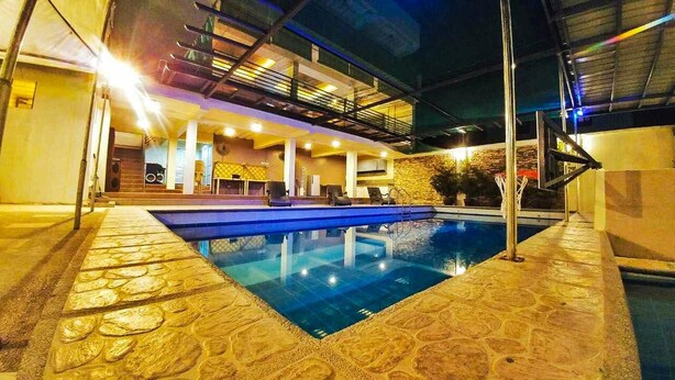 Una piscina interior con suelo de piedra, una zona de estar hundida y una terraza superior cubierta con barandillas.