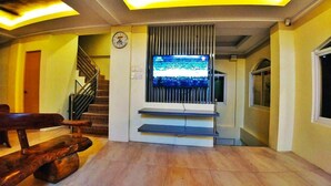 Una sala de estar con un televisor de pantalla plana grande montado en la pared, bancos de madera, una escalera y un reloj.