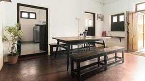A room with a wooden table and bench, a potted plant, and a refrigerator. - Laika Heritage Stay by evaddo stays (Mysore)
