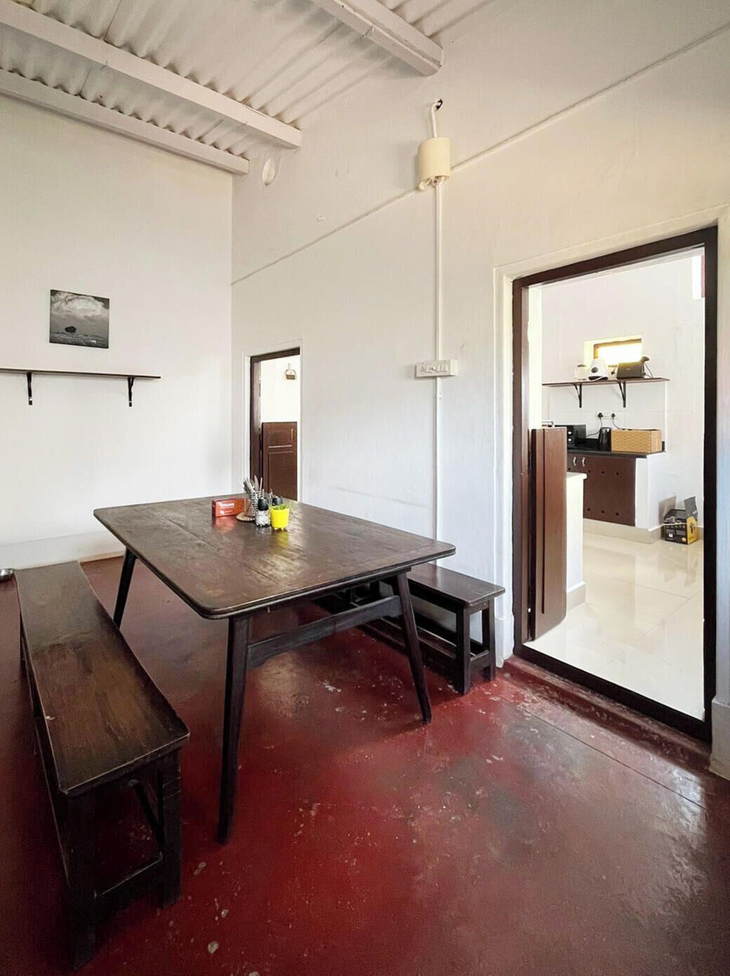 Una habitación con una mesa de madera, bancos, techo blanco y una puerta que da a una zona de cocina.