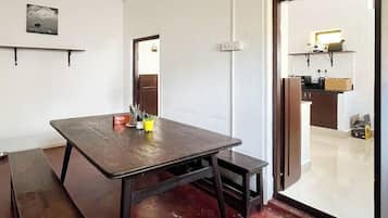 Una habitación con una mesa de madera, bancos, techo blanco y una puerta que da a una zona de cocina.