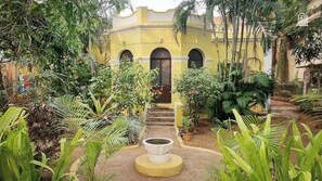 A courtyard with a yellow building, a central water feature, and lush greenery. - Laika Heritage Stay by evaddo stays (Mysore)