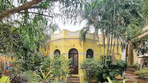 A courtyard with a central fountain, surrounded by lush greenery and a yellow building with arched windows. - Laika Heritage Stay by evaddo stays (Mysore)