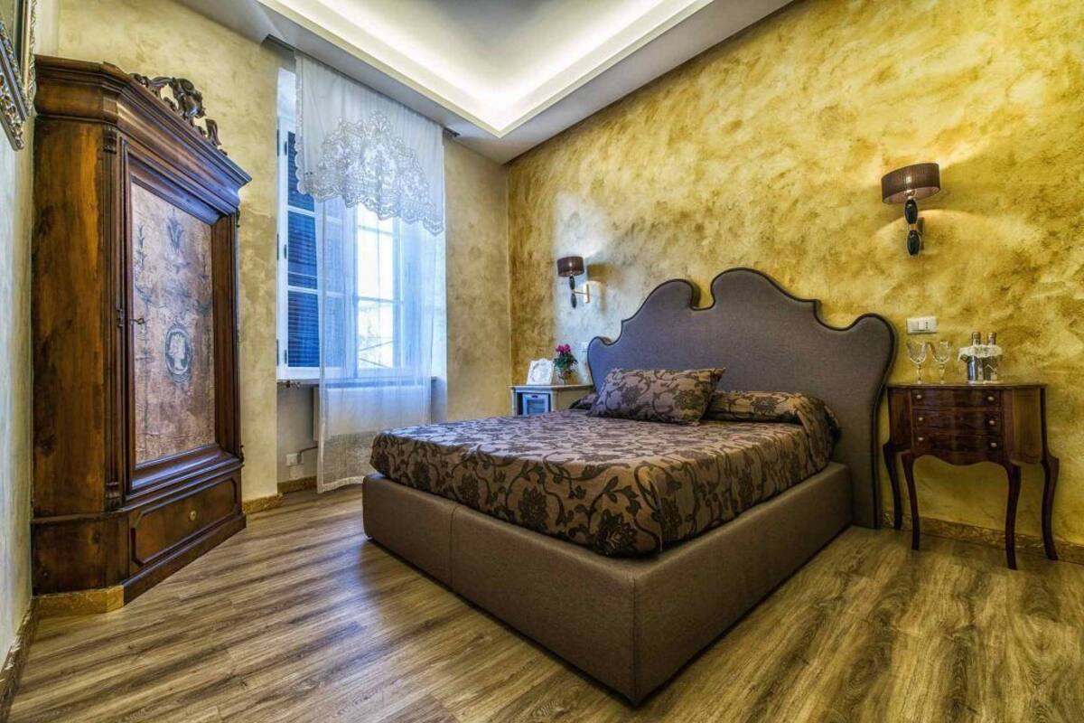 A bedroom with a large bed, wooden wardrobe, and a nightstand with a lamp.